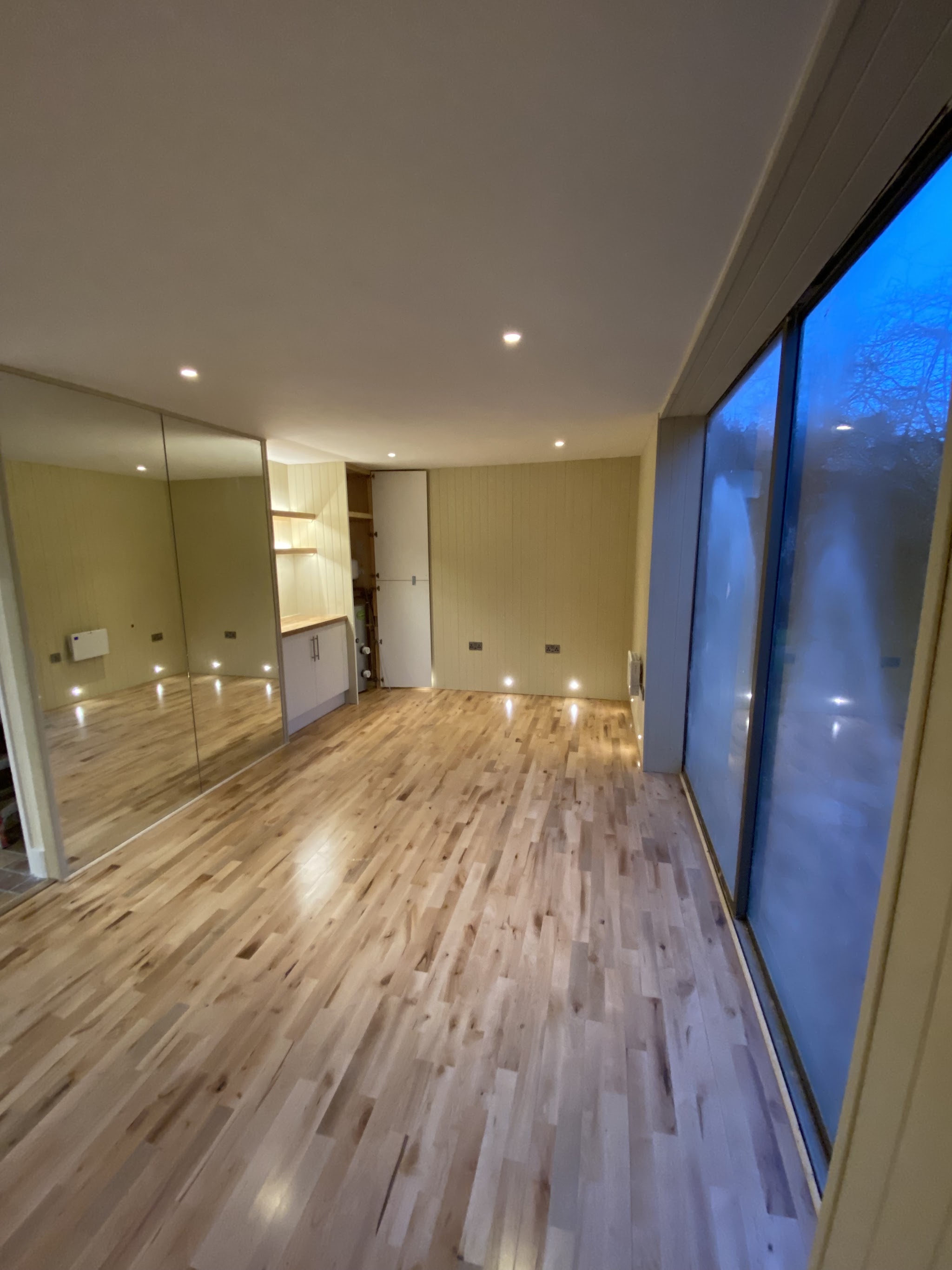 Long garden room at dusk lit by ceiling downlights and floor-level lights along an oak floor