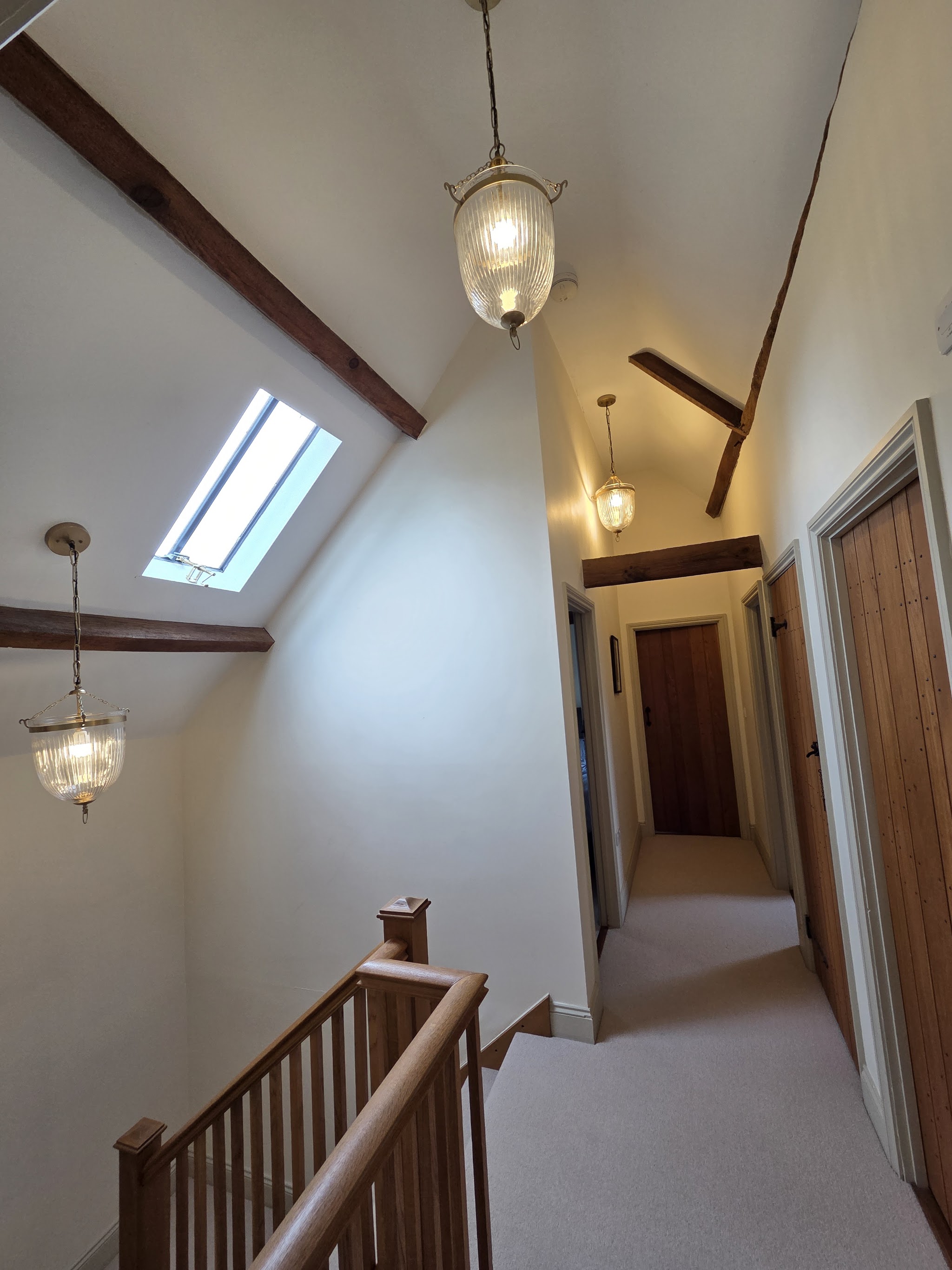 Vaulted landing with large glass pendant lights hanging between oak beams