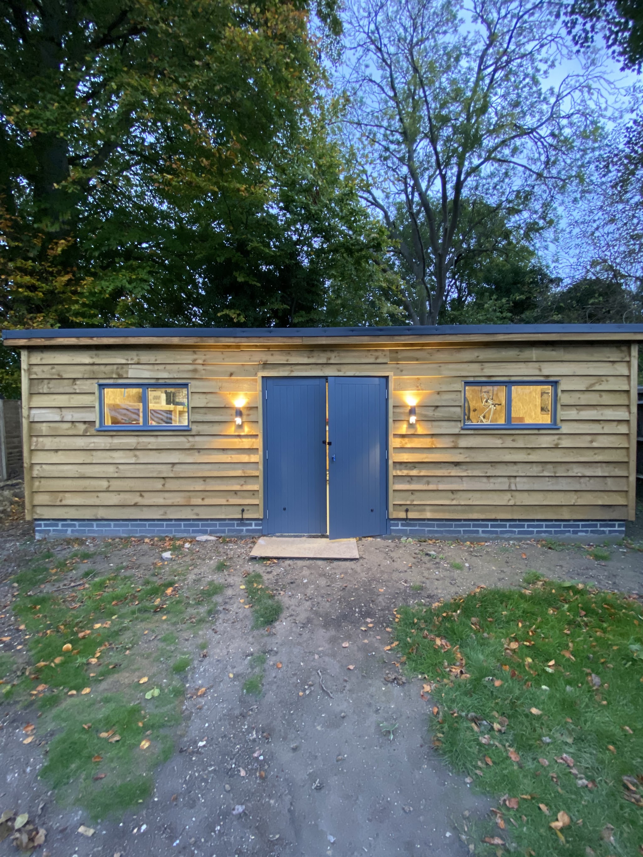 Timber garden building at dusk with two outdoor wall lights beside the doors