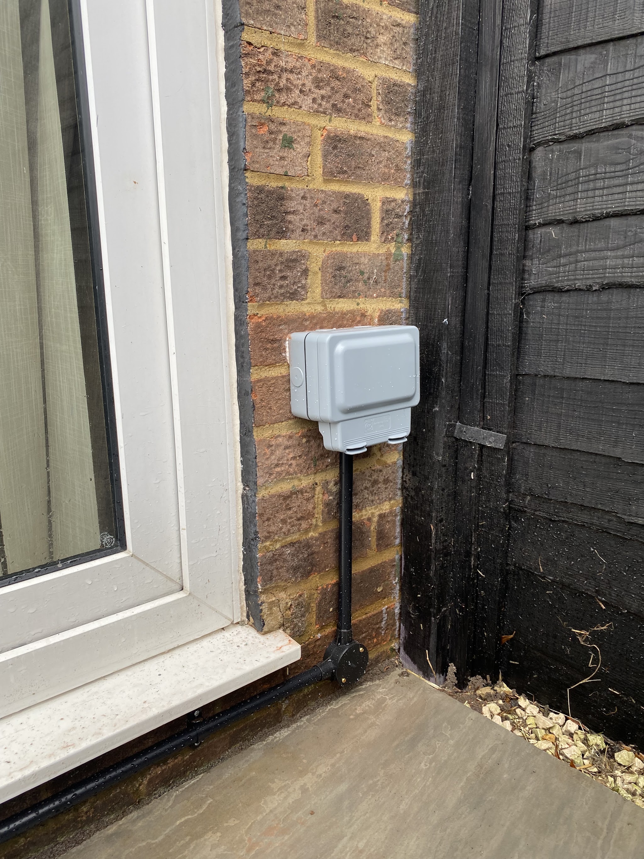 Weatherproof outdoor socket beside patio doors with the cable in black conduit