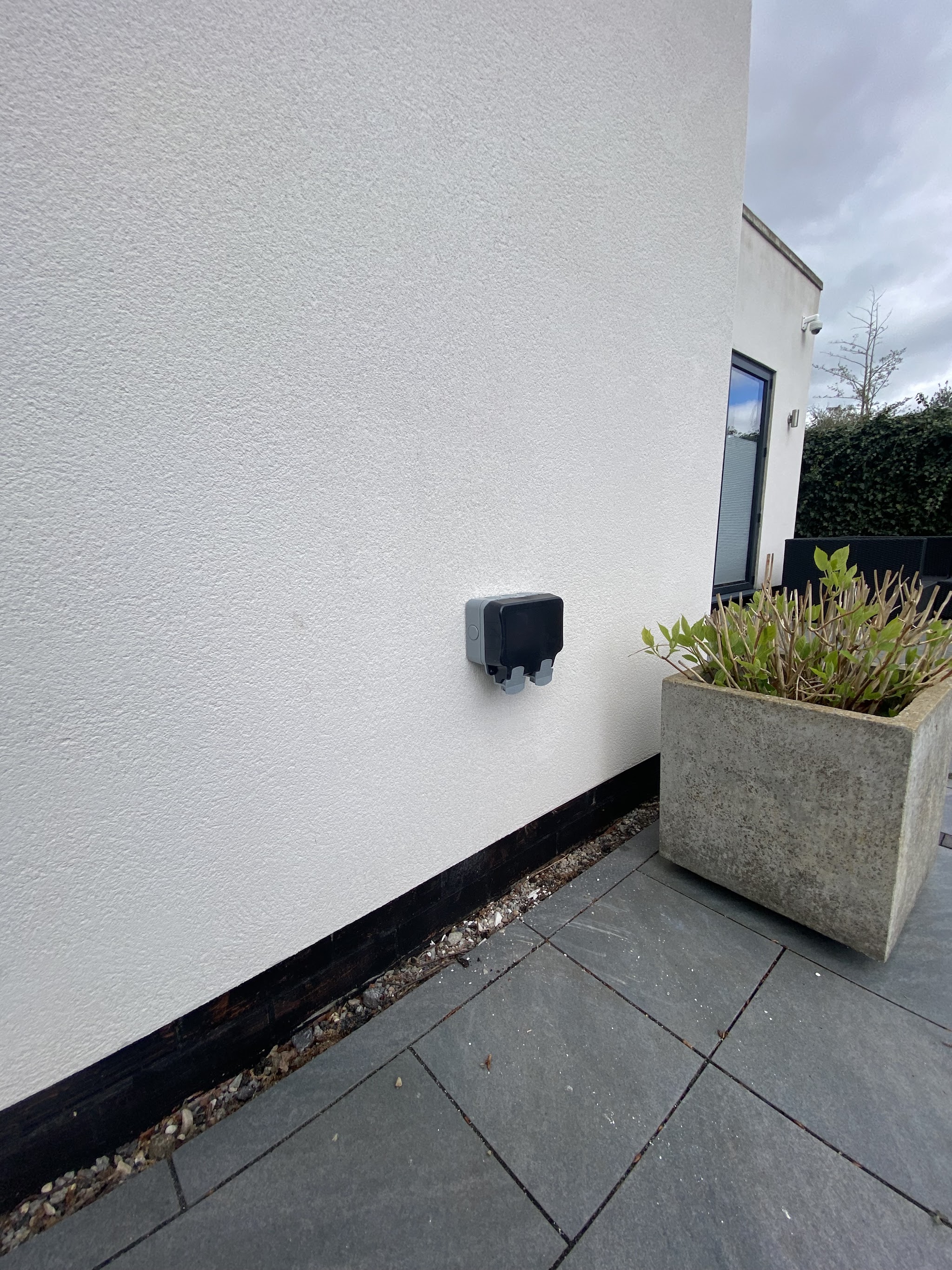 Outdoor socket on a white rendered wall next to a stone planter