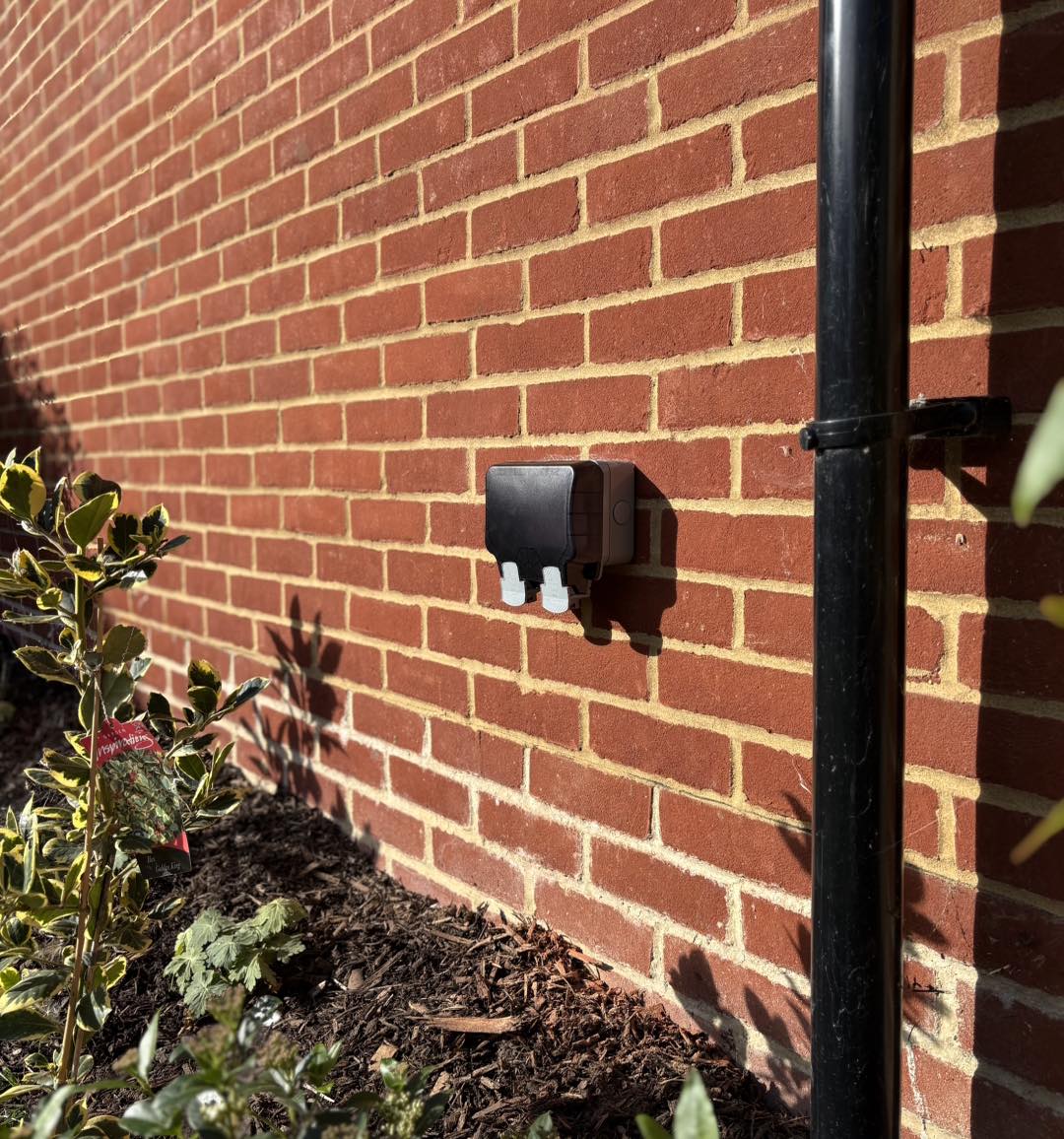 New weatherproof double socket on a red brick wall above a flower bed